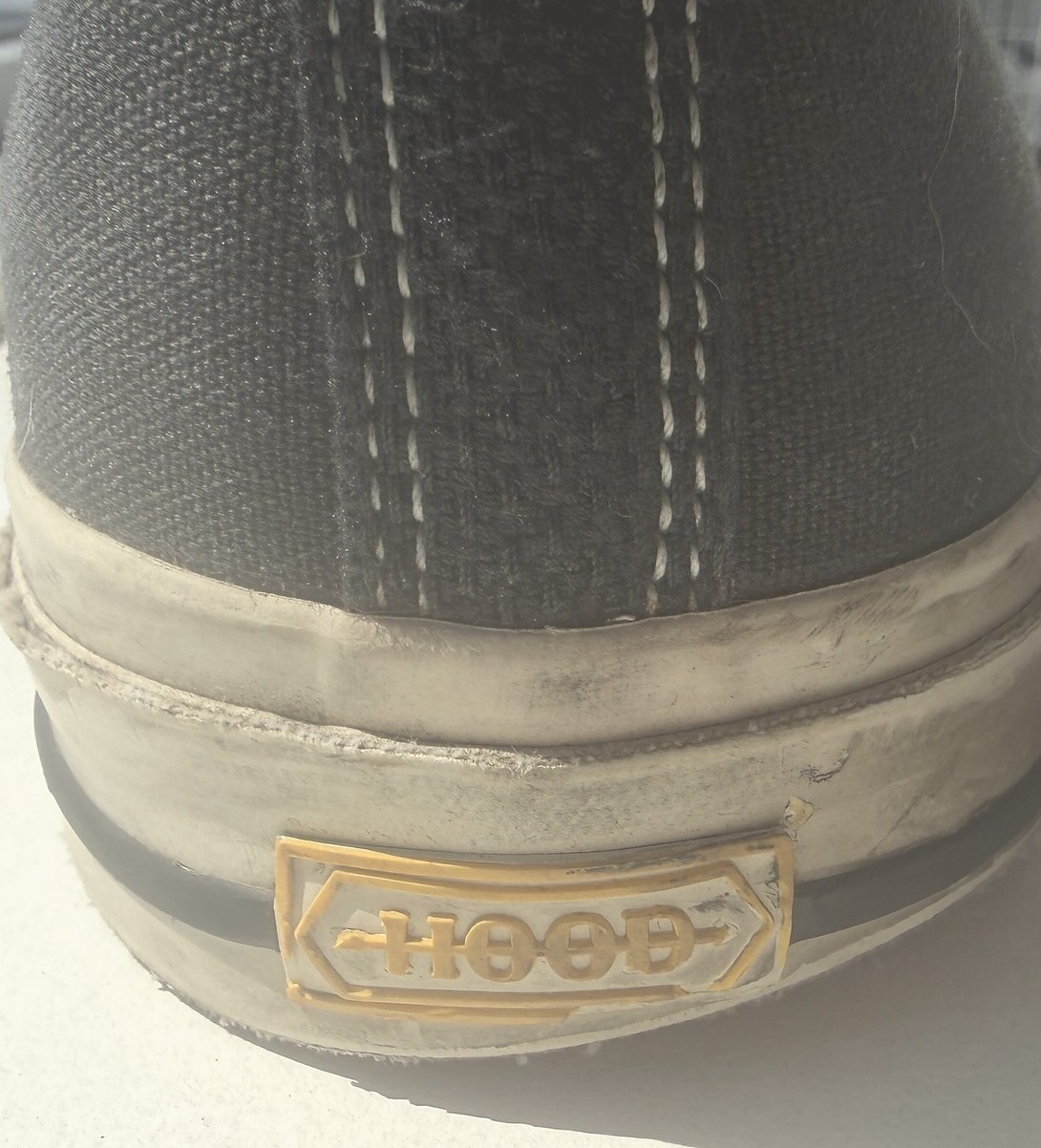 The back of a 1955 Hood Conference: twin rows of cream stitching down the heel seam, and a small amber rubber plate set into the foxing carrying the double-headed Hood arrow driven through the name.